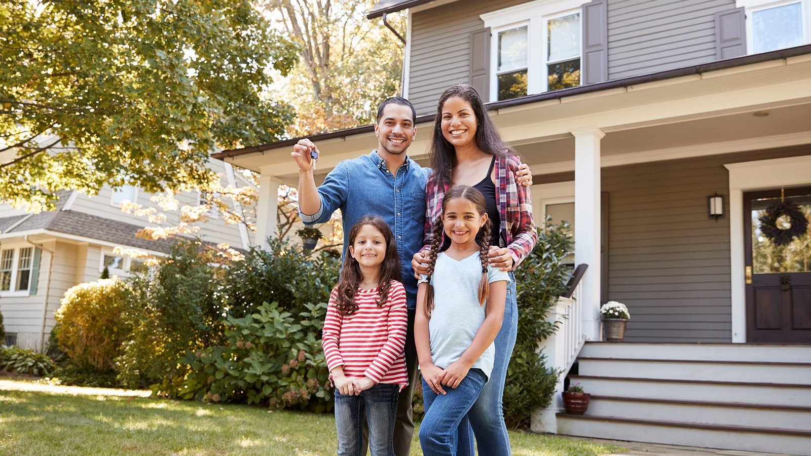 A family of four posing in front of house indicating home ownership