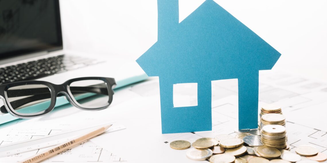 small house figurine, coins, laptop placed on the table indicating Property Valuation