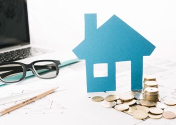 small house figurine, coins, laptop placed on the table indicating Property Valuation 