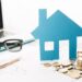 small house figurine, coins, laptop placed on the table indicating Property Valuation